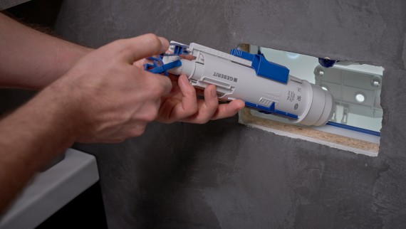 Vīrietis uzstāda Geberit noskalošanas vārstu zemapmetuma skalojamajā kastē (© Ben Huggler)